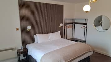 Un lit bien fait, avec une tête de lit, des tables de chevet, un porte-manteau mural, un miroir rond et un luminaire au plafond.