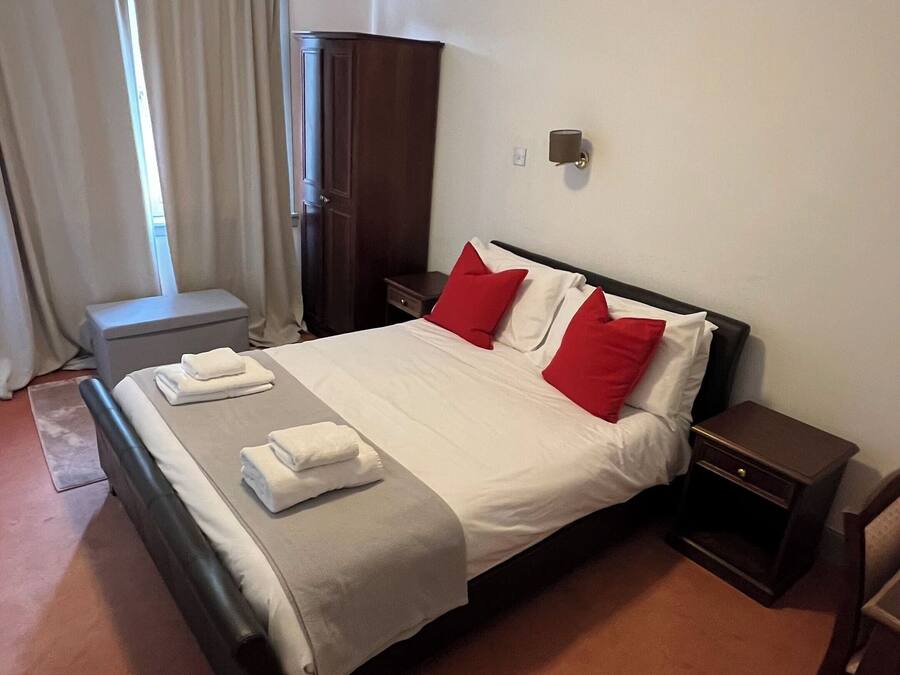 A hotel room with a bed, a nightstand, a wardrobe, and a window with curtains.