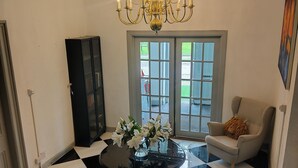 A room with a chandelier, a glass table with flowers, a black and white checkered floor, a white armchair, and a door with glass panels. - Hotel Square (Ballindalloch)