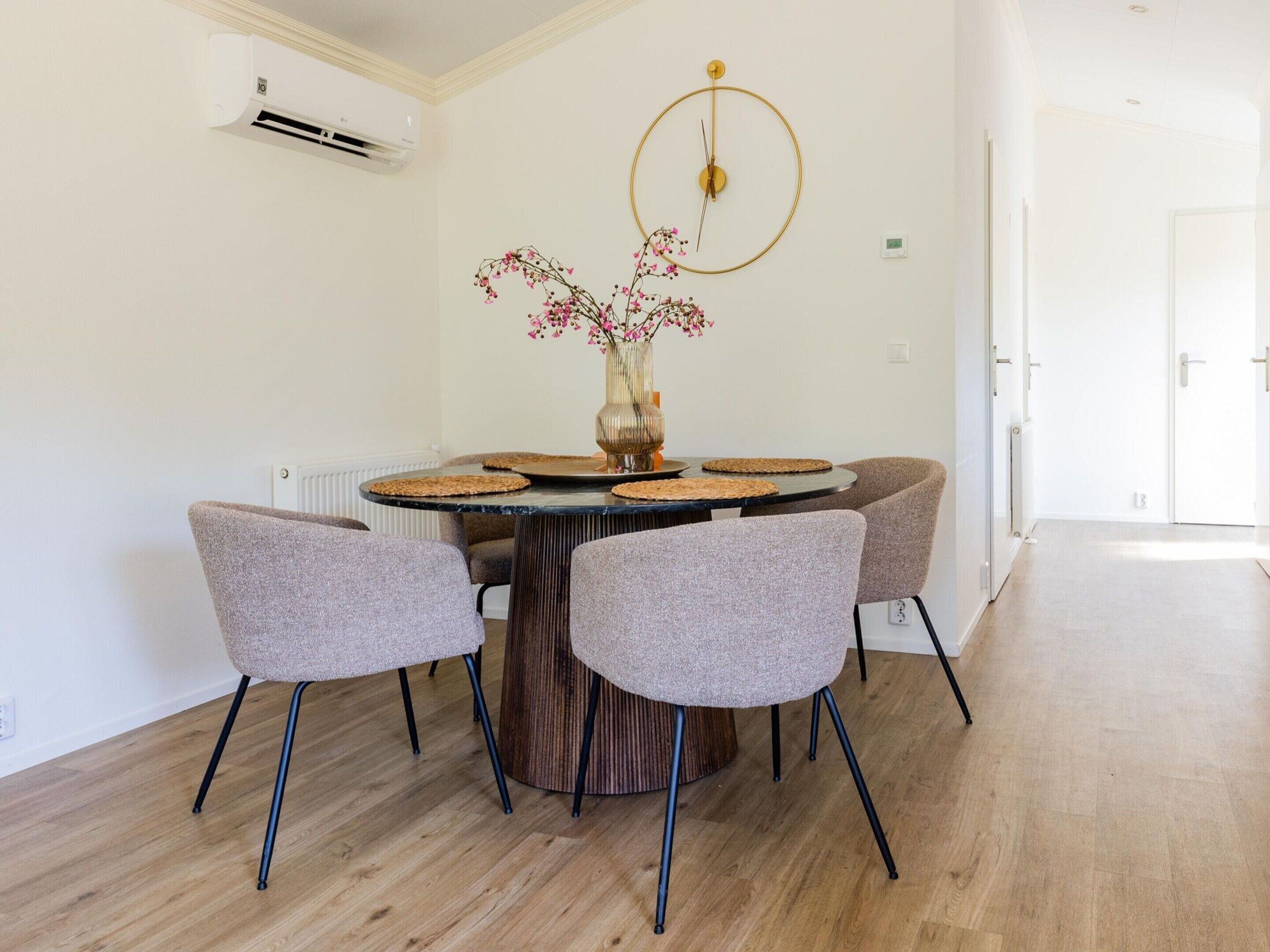 A dining area with a round table, four chairs, a vase with flowers, and a wall-mounted clock.