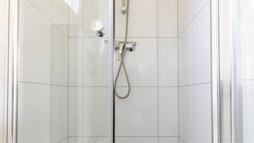 A glass-enclosed shower stall with a handheld showerhead and a wall-mounted control.