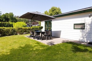 Une maison mobile blanche dotée d’un patio comprenant une table et des chaises, le tout installé sous un grand parasol.