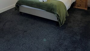 A neatly made bed with a green blanket and two rolled towels, flanked by two bedside tables with lamps, in a room with a dark carpet and a window with blinds. - Modern and stylish two bed room flat with a private balcony (Marston)