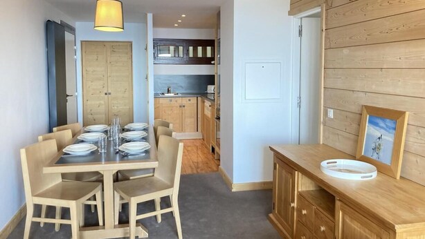 Una cocina compacta con muebles de madera y un comedor con una mesa dispuesta para cuatro.
