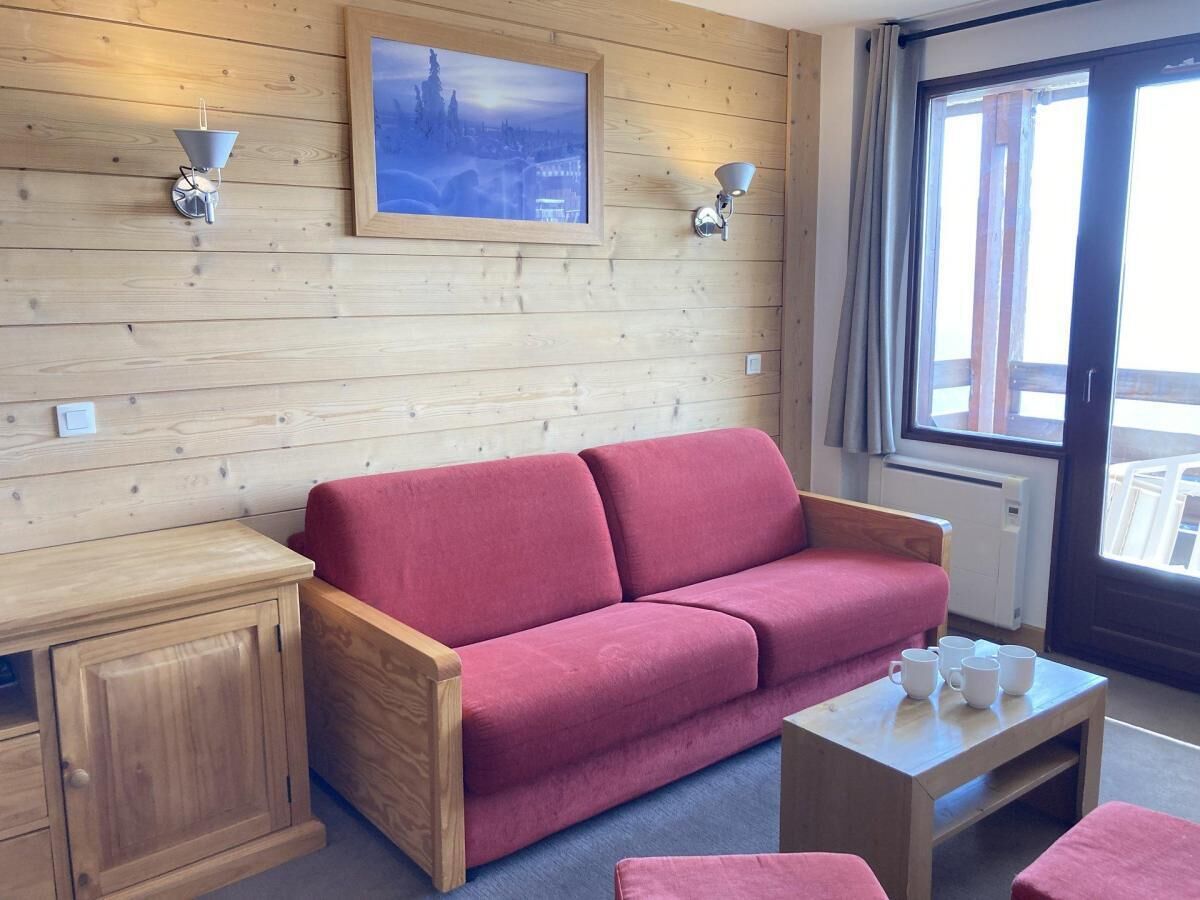 A wooden cabin interior with a red sofa, a small wooden table, and a framed picture on the wall.