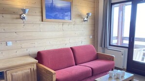 Interior de una cabaña de madera con un sofá rojo, una mesita de madera y un cuadro en la pared.