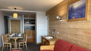 Una habitación acogedora con pared de madera, un sofá rojo, una mesa de comedor con sillas y una cocina al fondo.