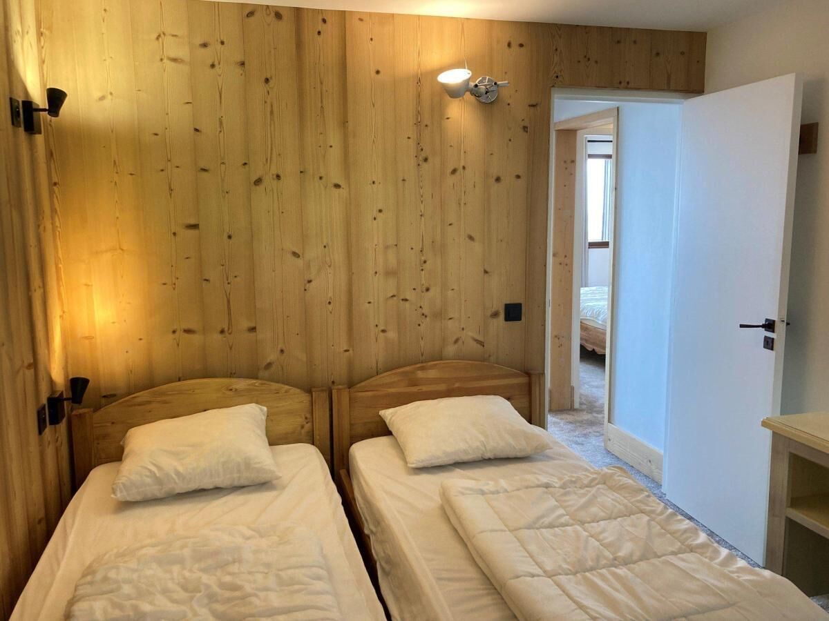 A room with two beds against a wooden wall, a nightstand, and a door leading to another room.