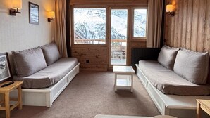 Ett mysigt rum med två soffor, ett litet bord och utsikt över snöklädda berg genom stora fönster.