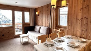 Ett rum med träpanel på väggarna, ett matbord för fyra personer, en soffa och ett fönster med gardiner.