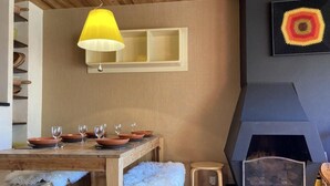 A dining area with a wooden table set for four, a yellow pendant light, and a fireplace with a modern design. - 10m from ski slopes, 2nd floor, view ski slopes, balcony, fireplace or stove, tv, 50m², Avoriaz (Avoriaz)