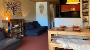 A cozy living room with a sofa, a wooden dining table set with plates and glasses, a lamp, and a wall with a decorative piece. - 10m from ski slopes, 2nd floor, view ski slopes, balcony, fireplace or stove, tv, 50m², Avoriaz (Avoriaz)