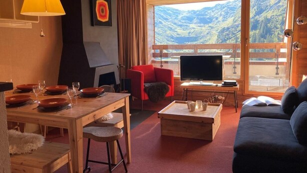 A cozy living room with a dining table set, a red armchair, a sofa, a TV, and a large window with a mountain view. - 10m from ski slopes, 2nd floor, view ski slopes, balcony, fireplace or stove, tv, 50m², Avoriaz (Avoriaz)