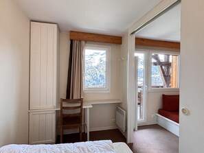 Ein Schlafzimmer mit Bett, Schreibtisch, Stuhl, Fenster mit Aussicht und einer roten Bank am Fenster.