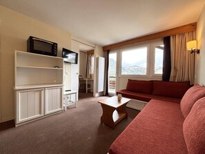 Une chambre dâhĂŽtel Ă©quipĂ©e dâun canapĂ©, dâune tĂ©lĂ©vision, dâun four Ă micro-ondes, dâune petite table et offrant une vue sur lâextĂ©rieur.