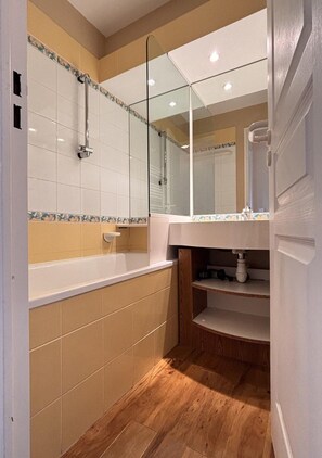 Ein Badezimmer mit einer Badewanne, einem Spiegel und einem Ablagefach unter dem Waschbecken.