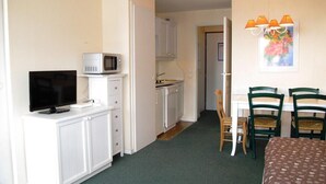 Habitació d'hotel senzilla amb bugateria, televisió, zona de menjador amb cadires i llit.