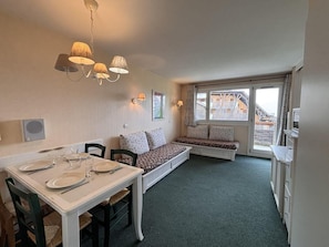Une pièce compacte comprenant une table à manger pour deux personnes, un banc avec des coussins, un banc intégré avec des coussins, une fenêtre avec des rideaux et un luminaire au plafond.