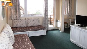 Habitació acollidora amb un llit, una banca, una televisió i una finestra amb cortines.