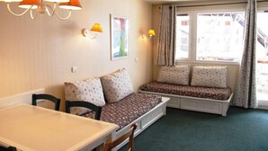 Habitació petita i acollidora amb taula de dinar, dues mences i finestra amb cortines.
