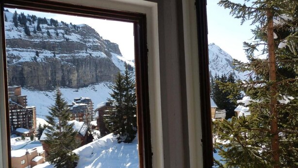 Vista a través de una ventana de un paisaje montañoso nevado con edificios y árboles.