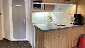 Una cocina compacta con armarios de madera, un microondas, una cafetera y un lavamanos pequeño.