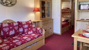 A cozy room with a wooden bunk bed, a red sofa with heart patterns, a wooden cabinet, and a small table with a glass.