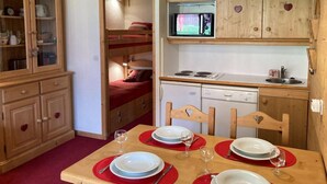 A compact room with a bunk bed, a kitchenette, and a dining area with a table set for two.