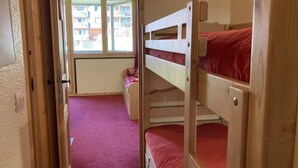 A room with bunk beds, a small desk, and a window with a view of buildings.