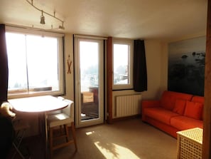 Ein kleiner, heller Raum mit einem Tisch, einem Sofa und einem Fenster mit Blick auf Gebäude.