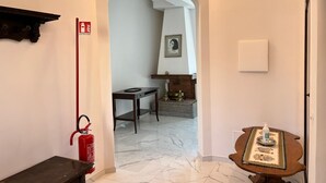 A hallway with a marble floor, a fire extinguisher, a small table with a decorative table runner, and a framed portrait on the wall. - Three bedrooms, two bathrooms near St peter's Cathedral Area (Roma)