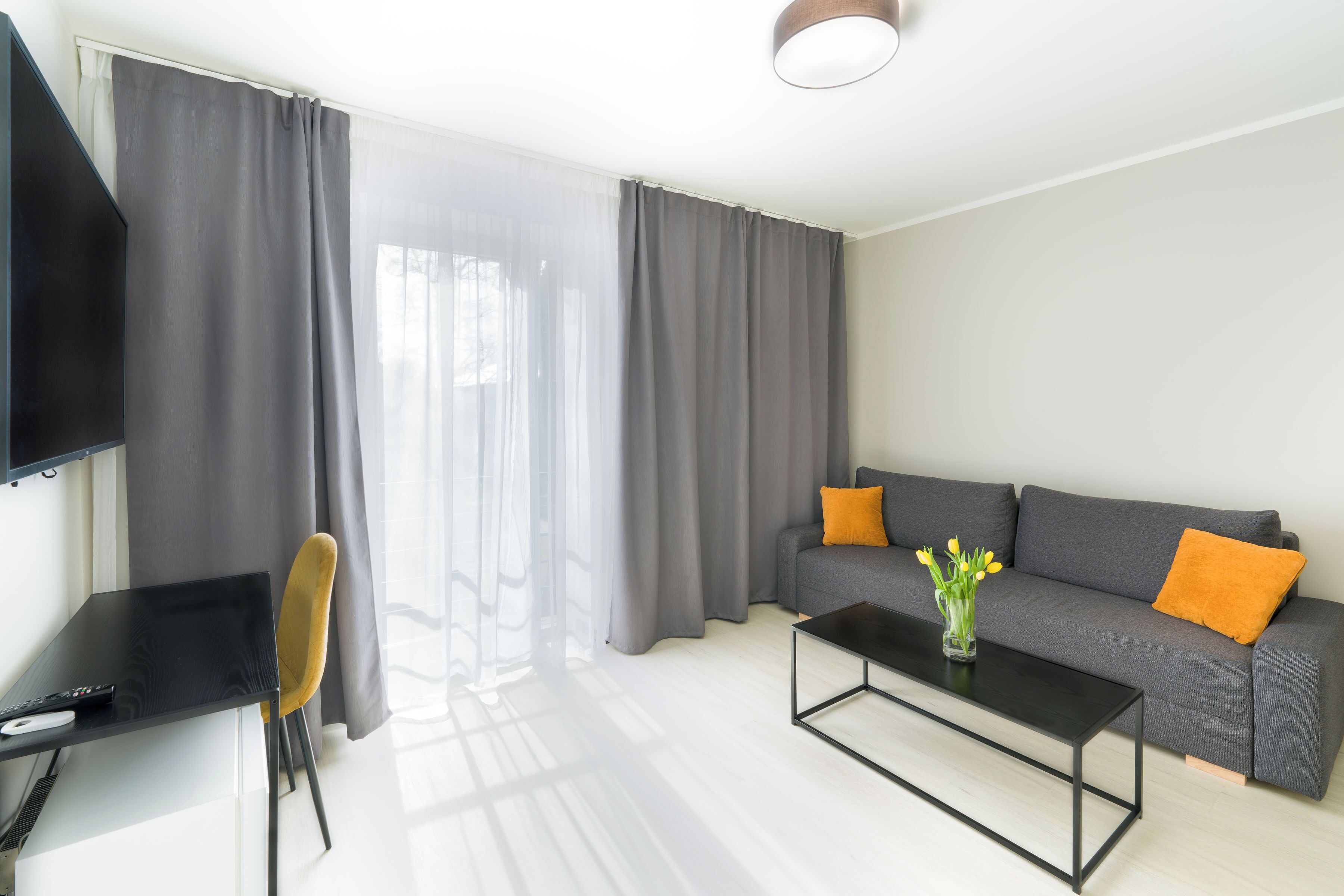 Een moderne woonkamer met een grijze bank, een zwarte salontafel en een gele fauteuil.