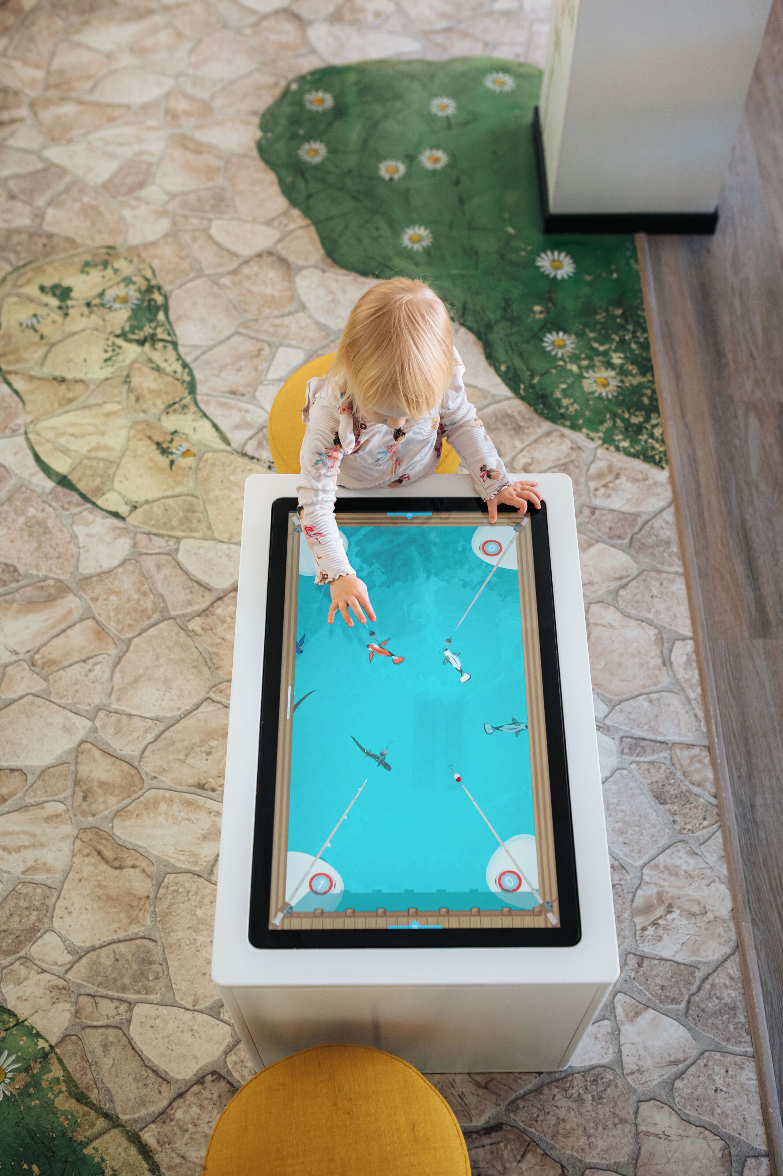 A child playing a pool game at a table with a stone floor and a green floral rug.