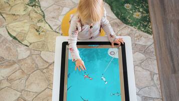 A child playing a pool game at a table with a stone floor and a green floral rug.