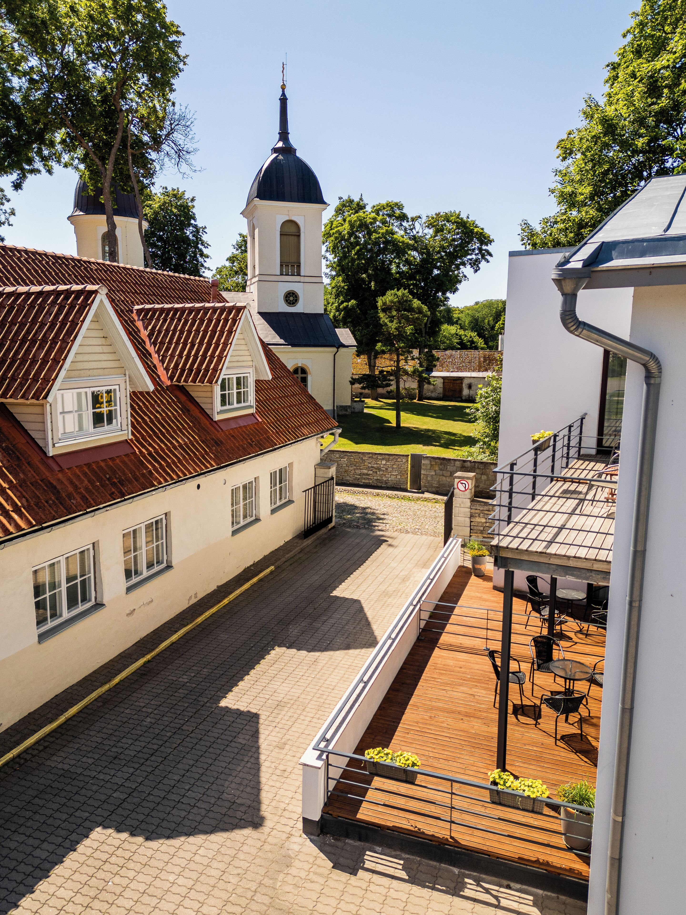 A courtyard with a traditional building featuring a tower and a dome, surrounded by trees and a paved walkway.