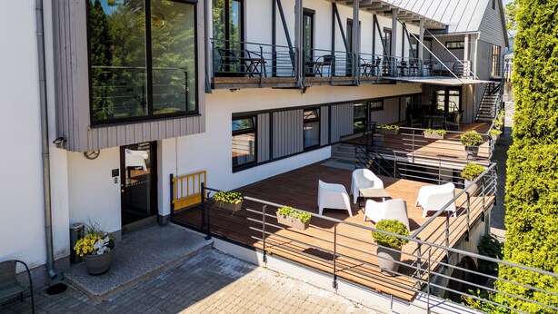 A modern building with a wooden deck, outdoor seating, and a staircase leading to an upper level. - Hotel NOSPA (Kuressaare)