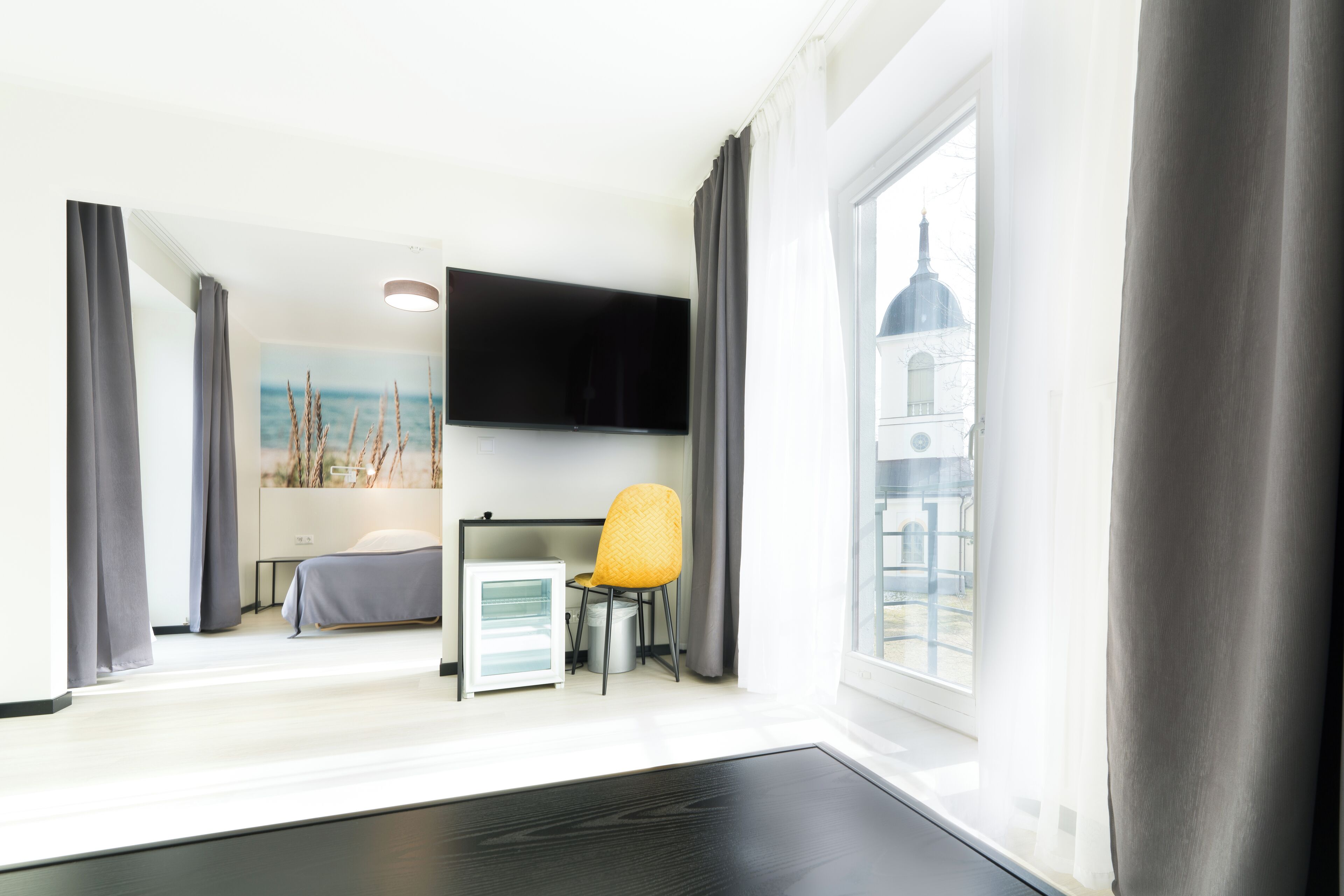 A hotel room with a bed, a small desk with a chair, a flat-screen TV, and a window with a view of a building.