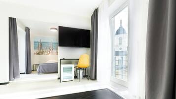 A hotel room with a bed, a small desk with a chair, a flat-screen TV, and a window with a view of a building.