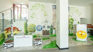 A lobby with a mural of a village scene, a staircase, and a modern reception desk. - Hotel NOSPA (Kuressaare)
