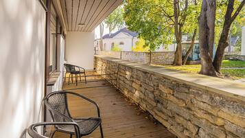 A covered outdoor area with a stone wall, wooden deck, and two wicker chairs.