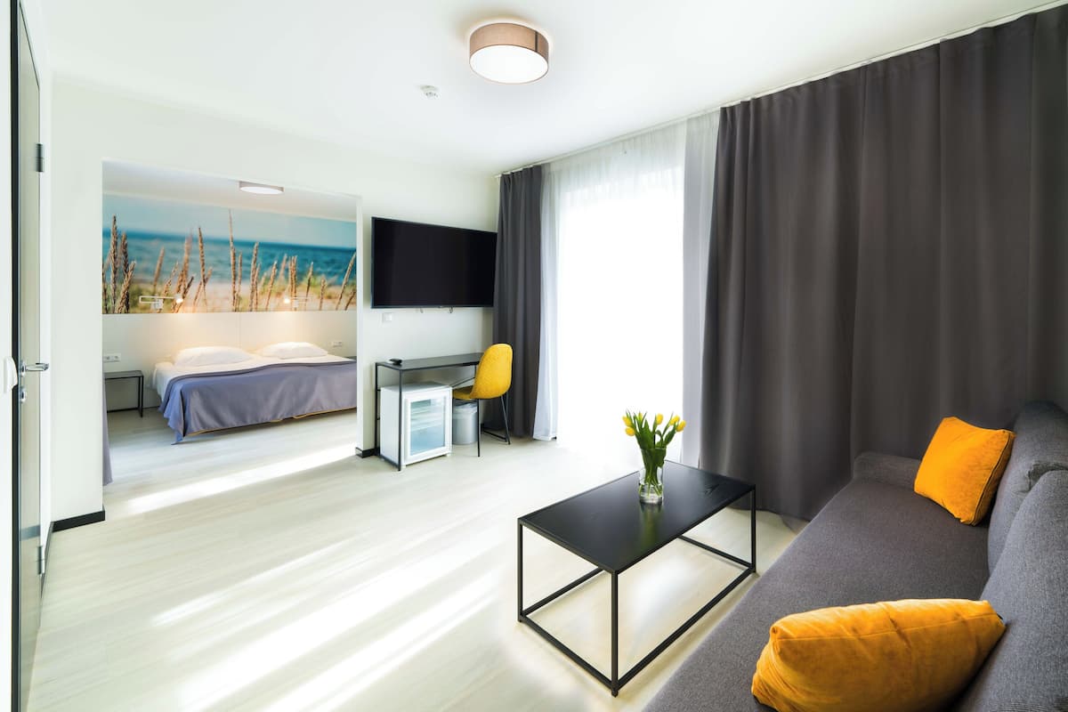 A modern hotel room with a bed, a desk, a sofa, and a flat-screen TV.