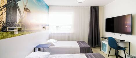 Habitación de hotel con dos camas, un escritorio, una silla, un televisor y un mural de molinos.