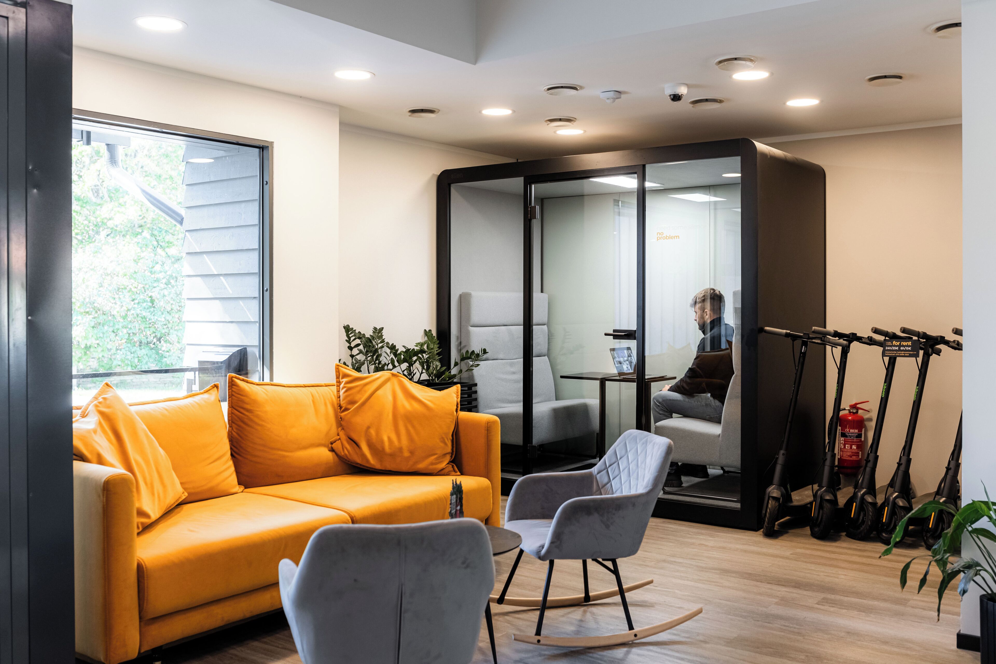 Um interior moderno com sofá, cadeiras, divisória de vidro e scooters elétricas.