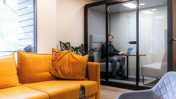 A modern office space with a glass partition, a yellow sofa, and a person working on a laptop.