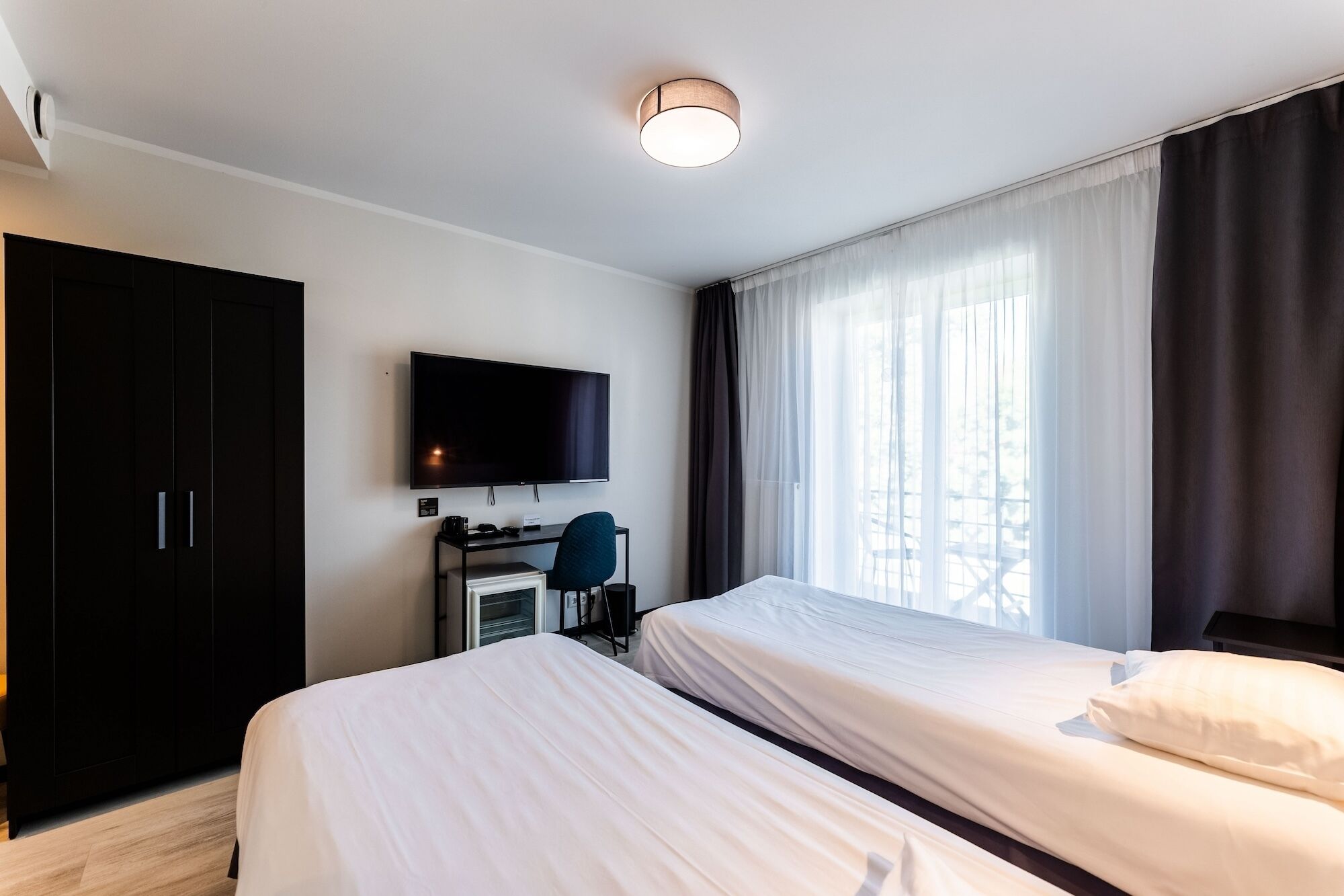 A hotel room with a bed, a desk with a chair, a television, and a wardrobe.