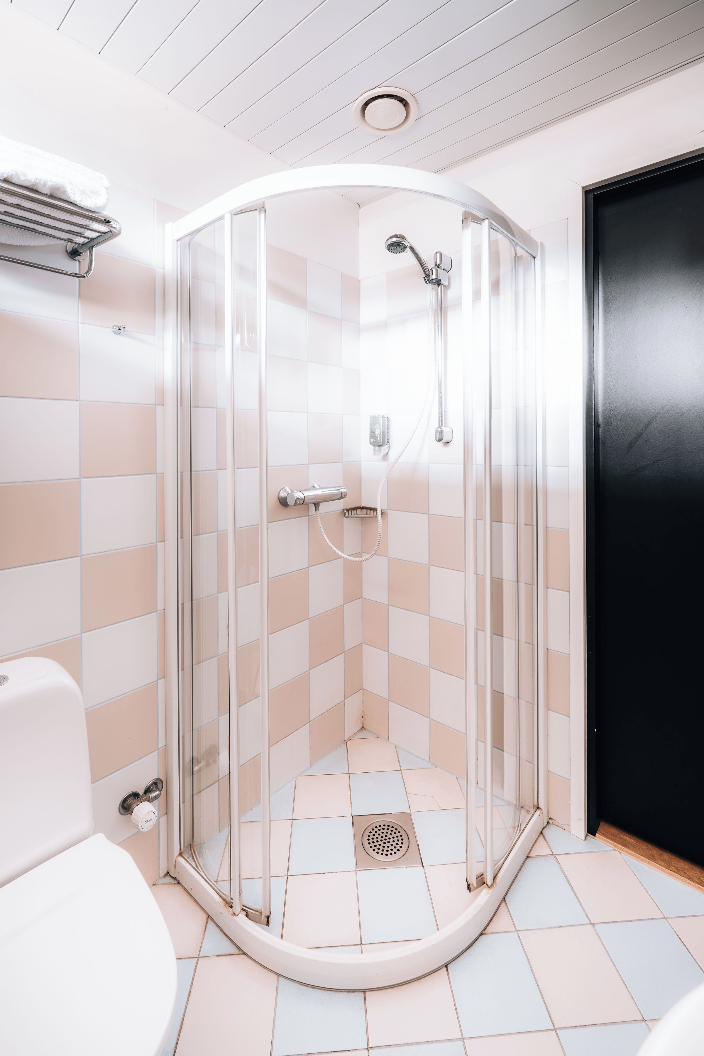 Un baño moderno con ducha envuelta en vidrio, azulejos blancos y una puerta negra.