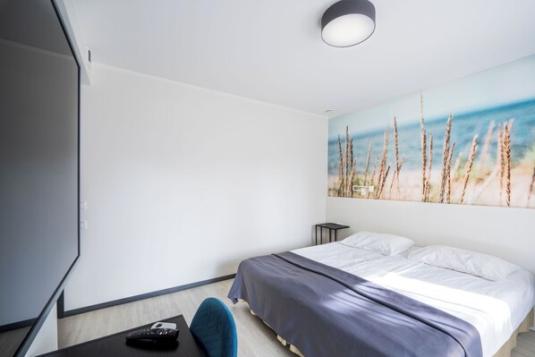 A modern hotel room with a bed, a desk with a phone, and a painting of a beach scene. - Hotel NOSPA (Kuressaare)