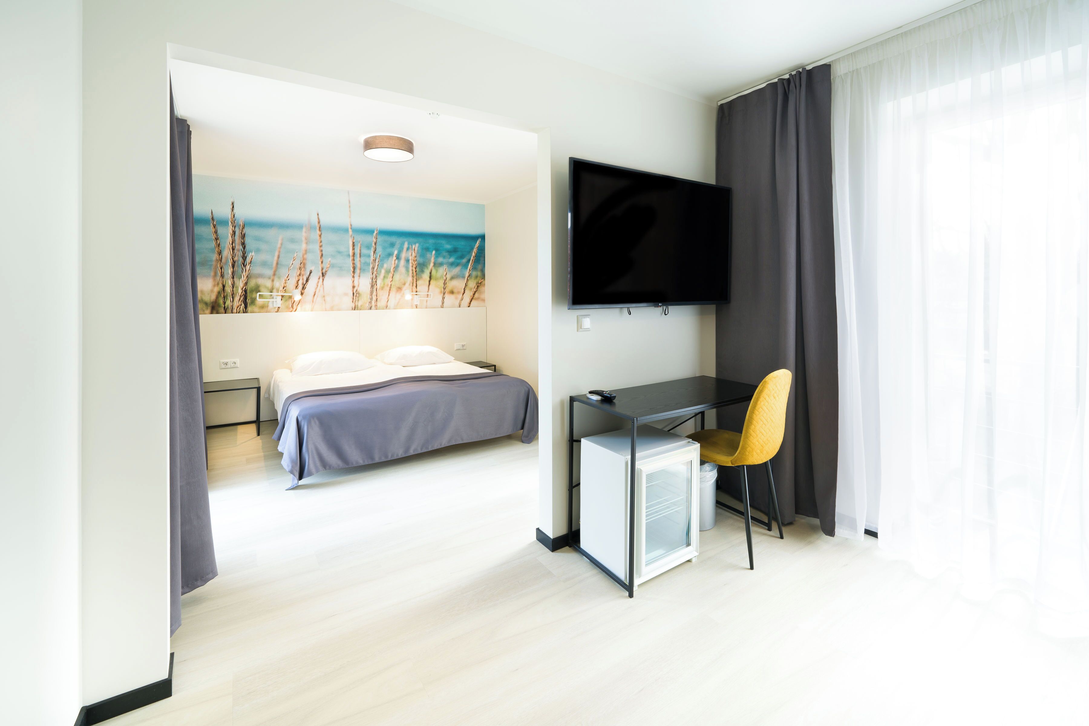 A modern hotel room with a bed, a desk with a chair, a television, and a small refrigerator.