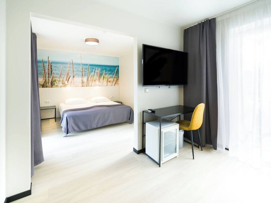 A modern hotel room with a bed, a desk with a chair, a television, and a small refrigerator.
