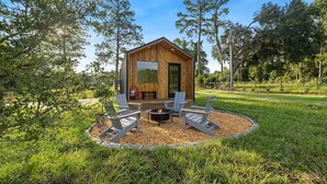 Una cabaña de madera con un hogar a leña y cuatro sillas Adirondack en un jardín ajardinado.